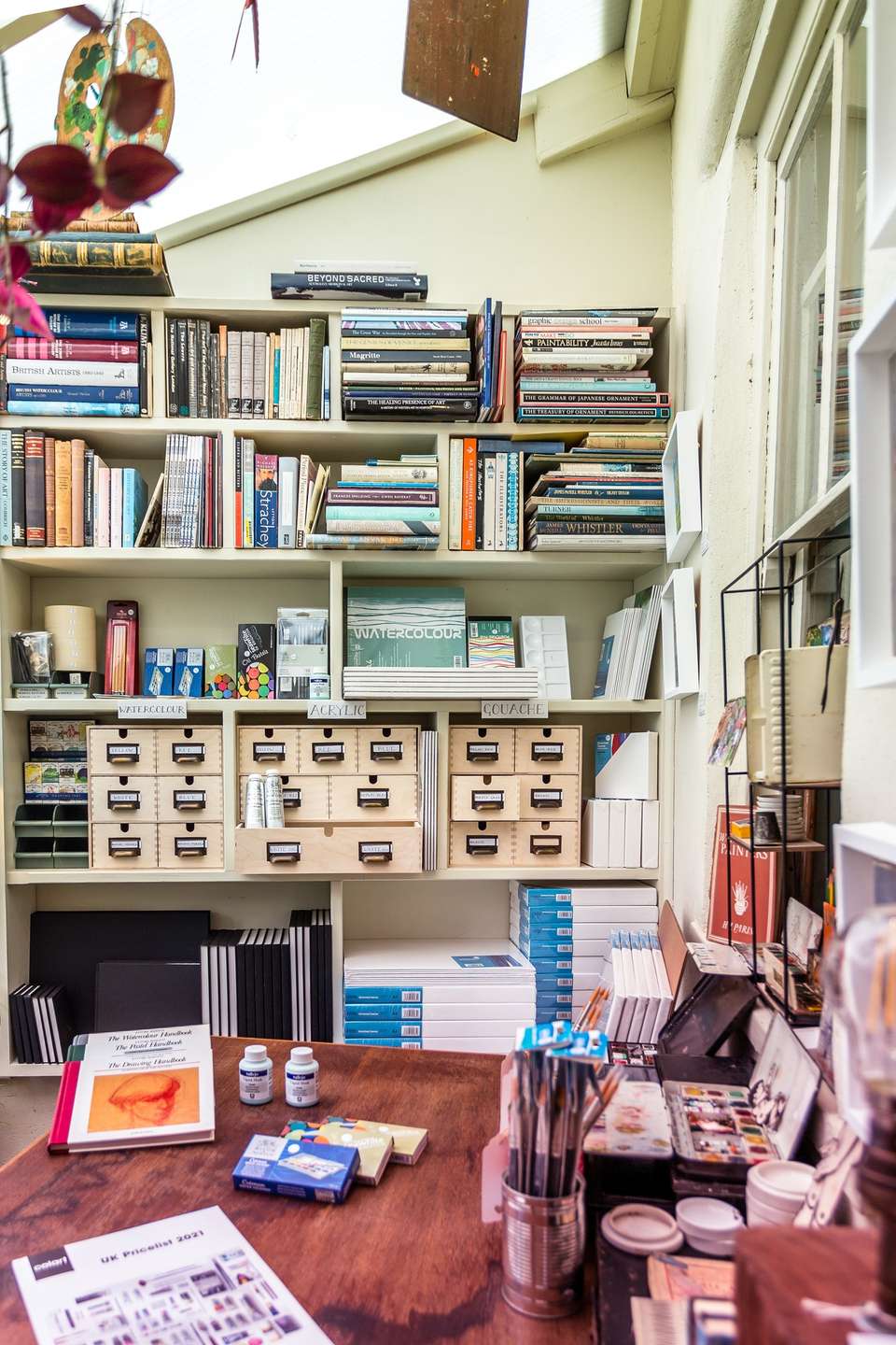 The art room: shelves of paints, sketchbooks and papers above a wooden counter