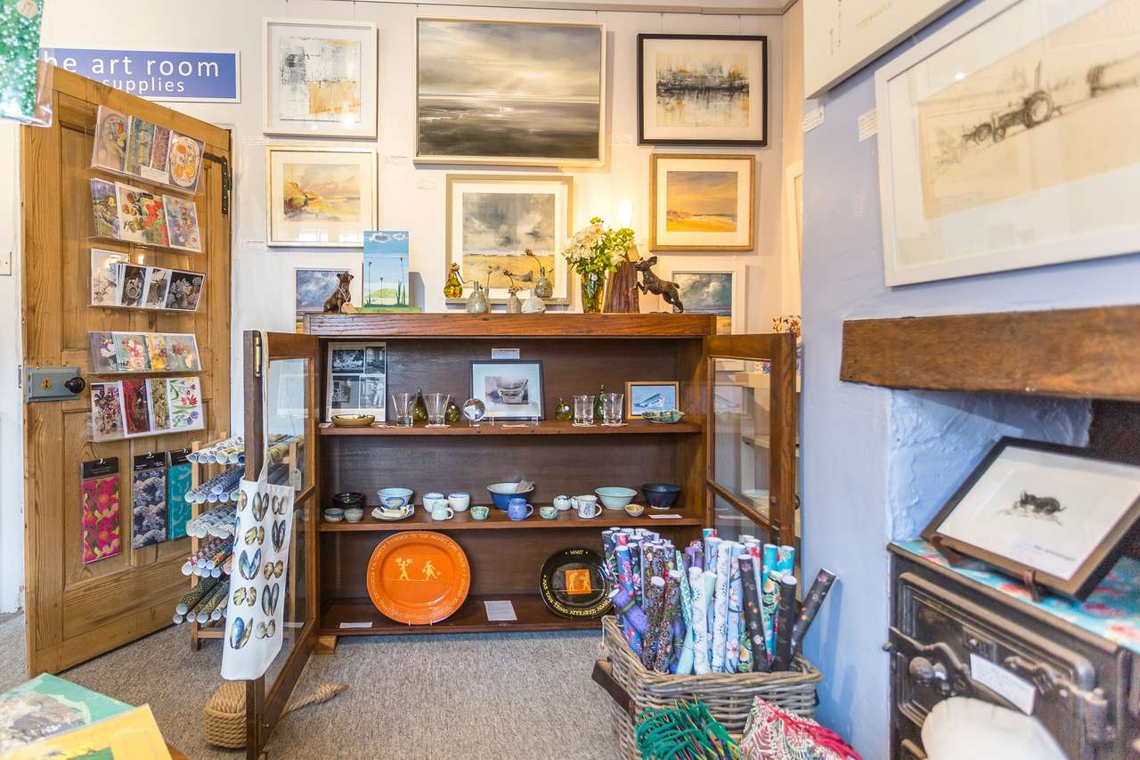 Inside the gallery: framed pictures on the walls, ceramics on a dresser and racks of cards
