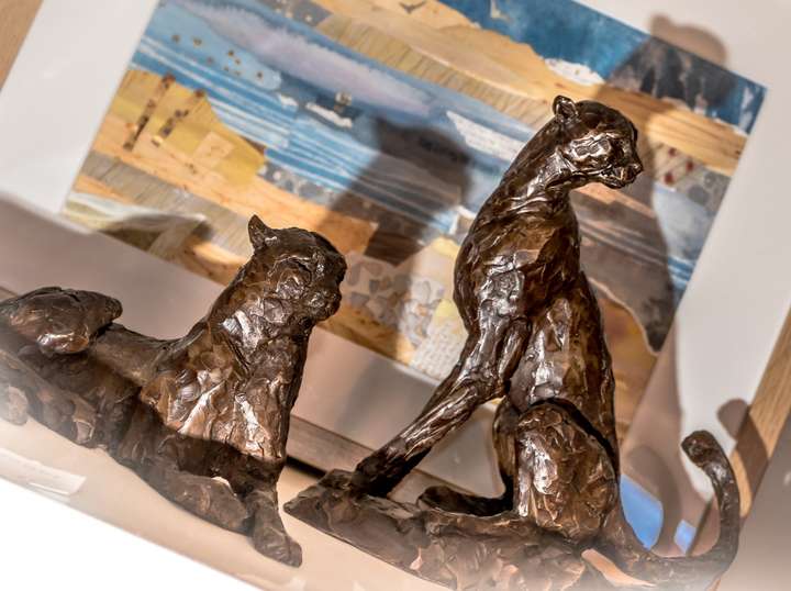 Two small bronze cat sculptures in front of a collage of the coast