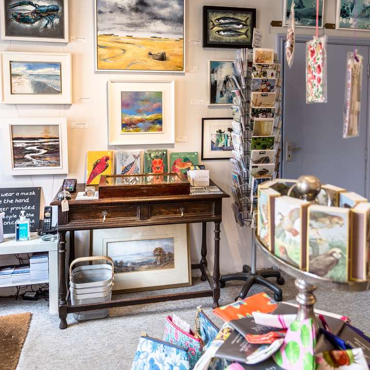A wall of framed paintings of the Norfolk coast above a writing desk